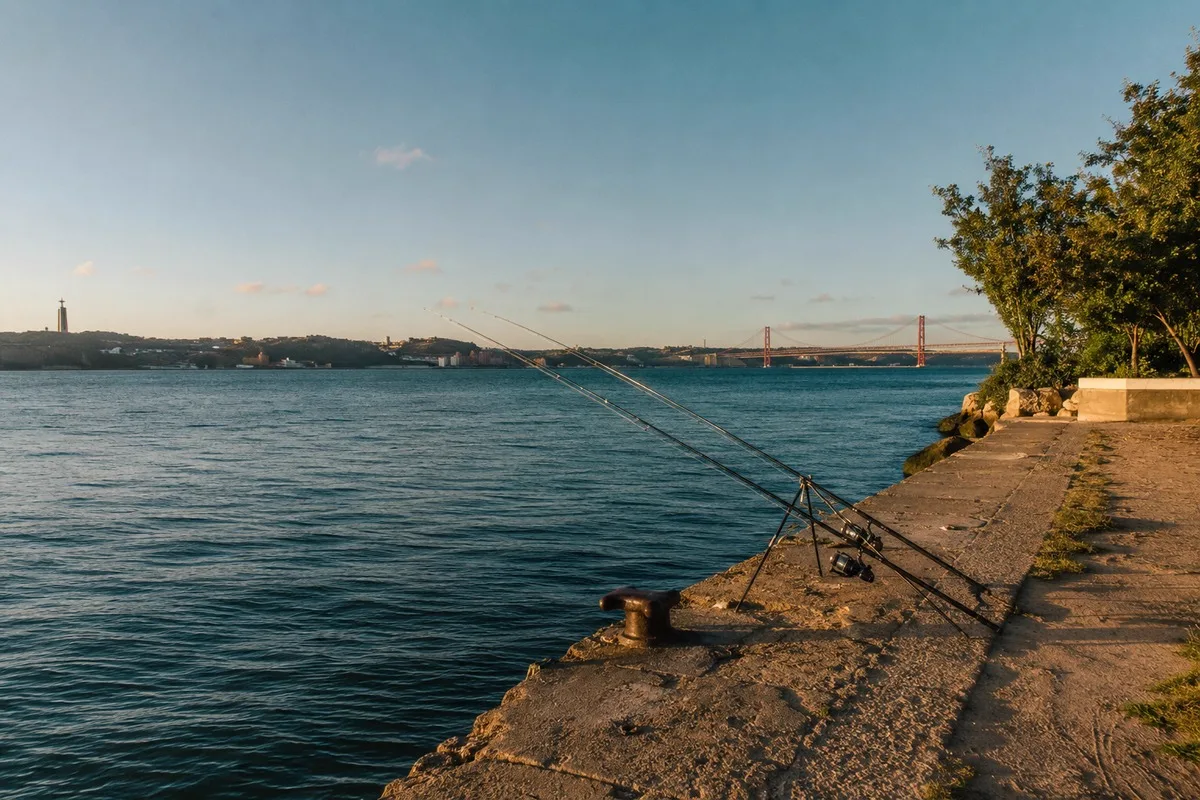 Frente ribeirinha do rio Tejo com canas de pesca e a Ponte 25 de Abril ao fundo